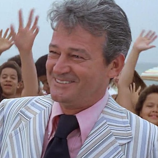 Production still from Jaws: Mayor of Amity smiles broadly during a TV interview about the shark attacks